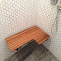 A teak ADA compliant L-shaped shower bench seat installed in a tiled shower stall.
